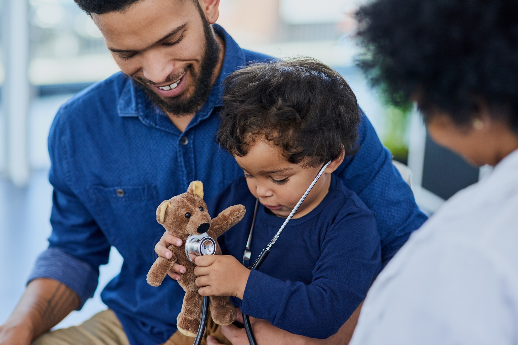 Dad with son holding a stuffed animal while visiting pediatrician 